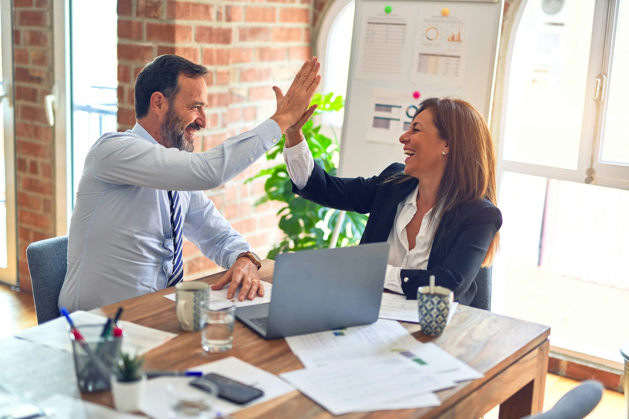 Two colleagues high-fiving at a desk after a success